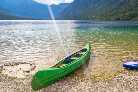 Green canoe with paddles rests on the pebbled shore of lake bohinj in slovenia, inviting visitors
