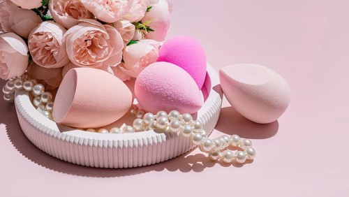 Various makeup egg sponges, a beauty blender, arranged amidst faux pearls and pink roses on a light