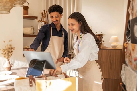 Two cheerful employees in a bag store using a tablet for checkout. They're standing behind the