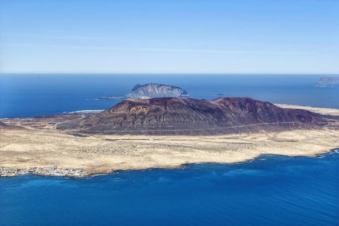 Dramatic volcanic island, La Graciosa, with barren surface, surrounded by deep blue ocean and