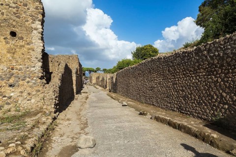 Long compacted crushed stone paved street with sidewalk and old stone walls plus residential