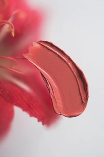 A vibrant smear of red lipstick is captured in a close-up, set against a softly blurred red flower