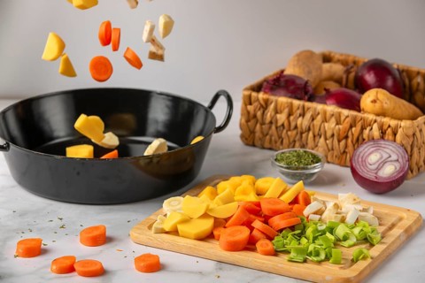 Vegetables fall into a black pot, next to fresh ingredients, soup vegetables and spices