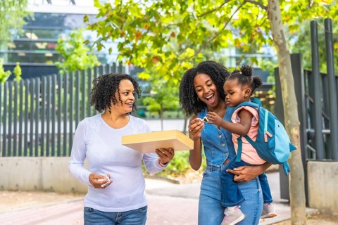 Three generation african female family in a public park carrying a girl and toys
