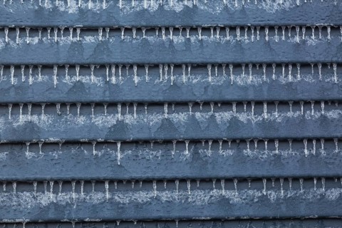 Close-up of exterior garden shed wall made of grey clapboard siding and covered with ice and