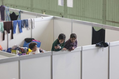 Children of refugees look over the wall of a temporary room in an emergency shelter for refugees on