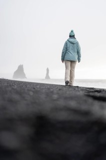 Back view of an unrecognizable of a solitary woman wanders towards the famous Reynisdrangar sea
