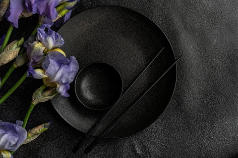 Top view of a sophisticated black dinnerware set complemented by delicate Iris flowers on a dark