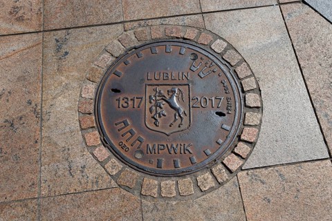 Bronze manhole cover with the coat of arms of Lublin and dates on paving stones, manhole cover,