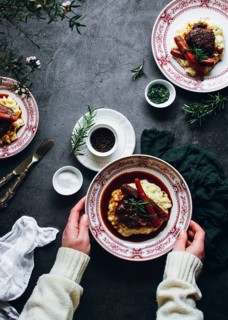 A deliciously plated beef dish with mashed potatoes, carrots, and fresh rosemary on a vintage