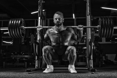 Image of a powerful athlete squatting with a barbell in a gym. Fitness and bodybuilding concept.
