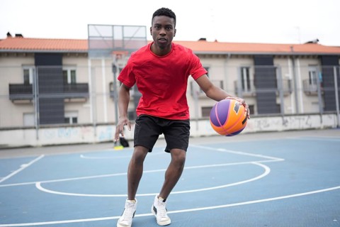 Frontal full length photo of an african basketball player dribbling in an outdoor basketball court