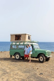 A joyful gay senior couple embraces beside an off-road vehicle during a scenic camping trip by the
