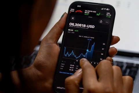 In this photo illustration, a person looks at a smartphone displaying Brent crude oil prices in