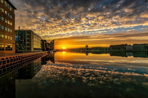 Farbintensiver Sonnenuntergang spiegelt sich im Wasser zwischen modernen Gebäuden, Kopenhagen,