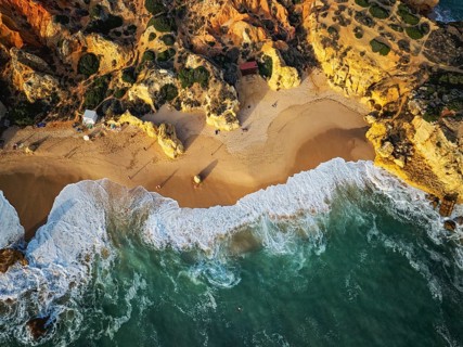 Drone top down view of Praia de Sao Rafael beach with foamy waves, sand, and golden limestone