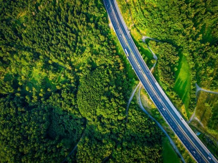 Aerial dramatc view to the road with lorry and many cars and green forest around in the summer.Alps