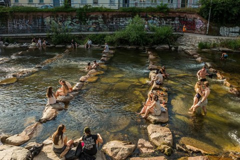 Young people sitting by and in the river, bathing in the city, heat, heat wave, climate change,