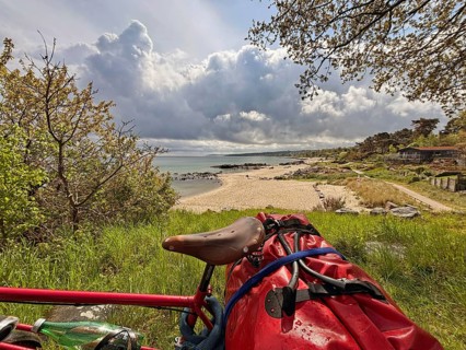 A bicycle stands on a hill overlooking a sandy beach and the sea under dramatic clouds, Allinge,