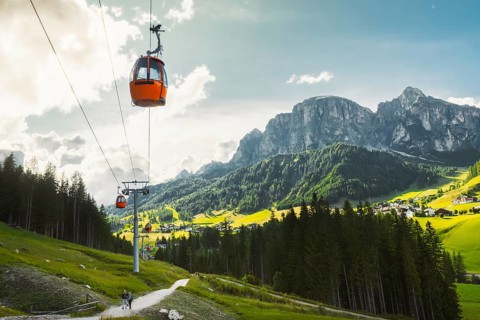 Dolomites, Italy - 27th july, 2026: Colfosco Orange cable car gondola lift ascending over lush