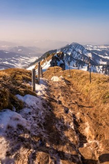 Snowy hiking trail on a mountain under clear, blue sky with distant views, Hochgrat Mountains,