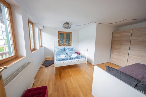 Minimalist bedroom with wooden bed and parquet floor, well lit through large windows, holiday