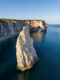 Aerial view of the distinctive Aiguille d'Étretat rock pin in the morning sun, behind it the La