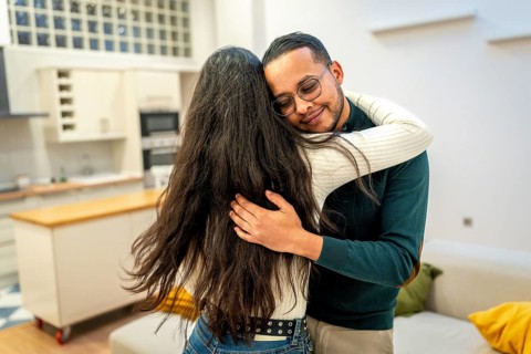 Multiracial couple sharing a warm, tender hug in their living room, showing affection, comfort and