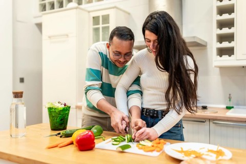 Young couple in a modern kitchen laughing as they chop fresh vegetables together on a cutting