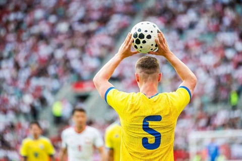 A soccer player wearing a yellow jersey with number 5 holding a ball over his head to perform a