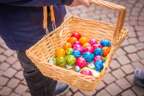 Woven basket with colorful Easter eggs is being held on a paved road, Easter campaign,
