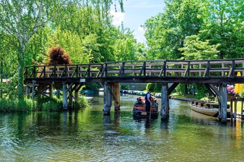 A boat with tourists sails under a jetty on one of the branches of the Spree in the Spreewald,