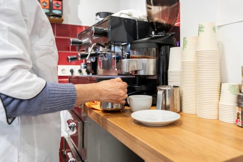 Barista hands operating a professional espresso machine, steaming milk in a metal jug next to