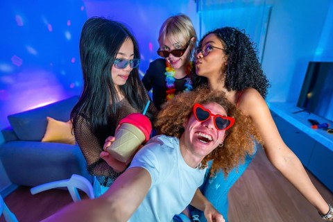 Group of cheerful multi ethnic friends taking a funny selfie at a neon lit home party, enjoying