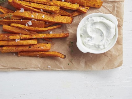 Close up view of roasted sweet potato sticks with yogurt and herbs sauce