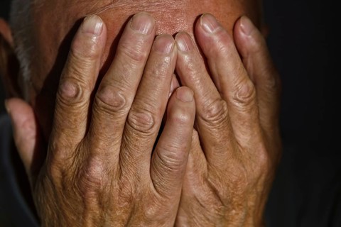 Close-up of a senior man's weathered hands gently covering his face, evoking emotions of