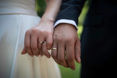 Close up of a bride and groom holding hands showing elegant gold wedding rings and a diamond