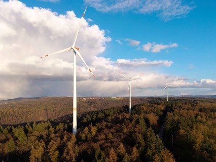 Wind turbines stand majestically above a wooded hill under a partly cloudy sky, wind turbine, near
