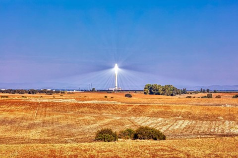 A solar tower rises above golden fields under a clear blue sky, solar thermal power plant PS10,