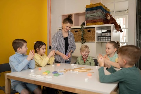 Children gather around a table for a creative lesson with a teacher. Smiling faces, bright colors,