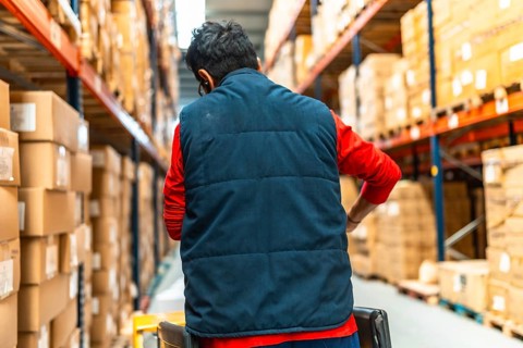 Rear view of a latin male worker pushing an hydraulic hand pallet truck on a warehouse