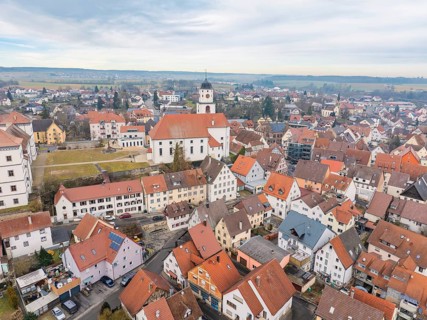 Aerial view of a small town with church and red tiled roofs, surrounded by rural landscape,