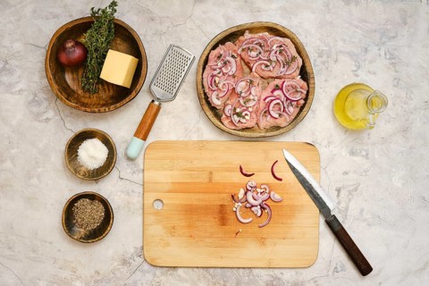 Fresh pork chops are arranged on a wooden plate with sliced onions and herbs nearby. A cutting