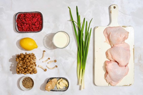 Three pieces of raw chicken on a cutting board. Next to them, there are mushrooms, herbs, berries,