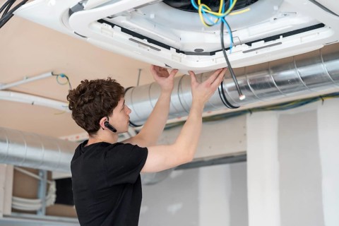 Young male technician installing a modern cassette air conditioning unit into a ceiling during