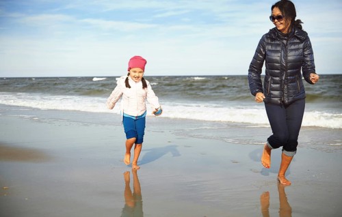 A joyful scene featuring a mother and daughter running barefoot on a sandy beach in California,