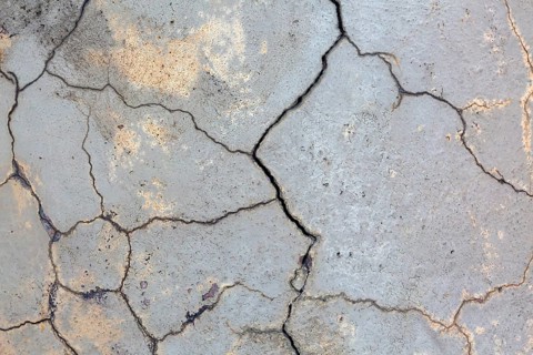 Close-up of multiple small cracks and deep fissures on grey painted concrete foundation exterior
