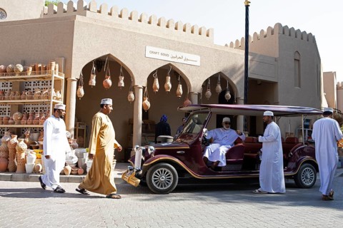 Omani men in traditional dress and a tourist vehicle in the souk or soug or market in the old town