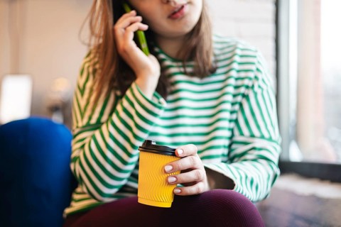 A cropped unrecognizable woman enjoys a coffee break in a cafe, holding a disposable cup and