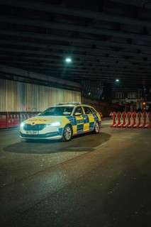 Police car in a cone of light stands in front of barriers under a bridge at night, New Year's Eve